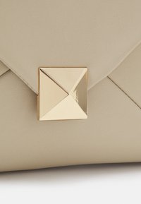 Beige faux læder clutch med et geometrisk guldtonet lås. Har en quiltet tekstur og vinklede designelementer.