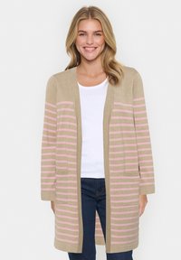 Beige lång kofta med rosa horisontella ränder, öppen framtill och sidofickor, bärs över en vit topp och mörka jeans. Mjuk textur.