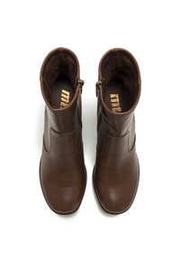 Stivali ankle in pelle marrone con esterno liscio, chiusura con cerniera e fodera interna confortevole. Presentano un tacco basso e una punta arrotondata.