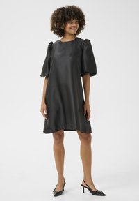 Svart satin klänning med lös passform, puffärmar och rundad halsringning. Stylande med svarta slingback-skor och en slät textur.