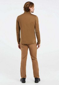 Brun långärmad topp och matchande byxor, båda gjorda av ett slätt, stretchigt material. Outfiten har en figurnära design och enkel logodetalj.