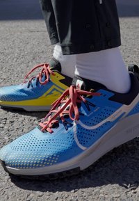 Scarpe da corsa blu con accenti neri e gialli, dotate di una tomaia in rete, perforazioni, lacci rossi e una suola durevole e testurizzata.