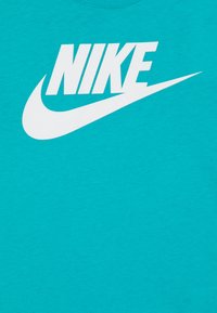 Tirkīza kokvilnas T-krekls ar lielu baltu "NIKE" logotipu un swoosh grafiku, ar apaļu izgriezumu un gludu tekstūru.
