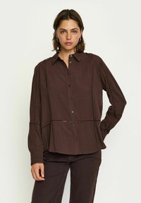Chemise marron à manches longues avec un devant à boutons, dotée de coutures contrastantes et d'une coupe décontractée, fabriquée en tissu léger.