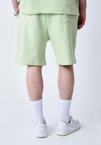 Shorts vert clair en tissu doux, dotés d'une poche arrière, associés à des chaussettes blanches et des baskets blanches.
