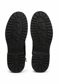 Suelas de botas negras con dibujos profundos que presentan patrones triangulares y el logo de "Tommy Jeans" grabado cerca del área del talón.