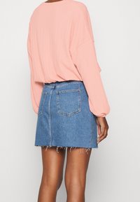 Vaaleanpunainen tekstitetty pitkähihaisen paidan yhdistelmä lyhyiden farkkuhameen kanssa, jossa on repaleinen helma ja takataskut. Kokonaisuus on rento.