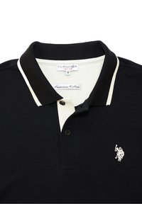 Polo negro hecho de algodón premium. Cuenta con un cuello blanco en contraste y una tapeta de tres botones. Pequeño logotipo en el lado izquierdo del pecho.