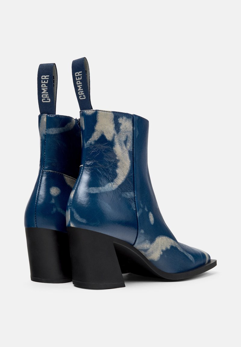 Blå läderankelboots med en glänsande yta, med ett unikt krämfärgat abstrakt mönster, fyrkantig tå och en kraftig svart klack.