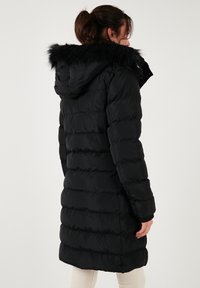Abrigo acolchado negro con capucha y borde de piel sintética, con un diseño acolchado y puños acanalados, que llega hasta la mitad del muslo.