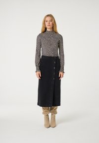 Langärmlige Bluse mit hohem Kragen und einem weißen Punktmuster auf schwarzem Hintergrund, kombiniert mit einem schwarzen Jeansrock mit seitlichem Knopfverschluss.