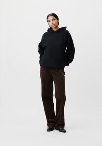 Felpa nera oversize con una texture morbida, abbinata a pantaloni in velluto a coste marroni. L'outfit include scarpe nere con una finitura liscia.