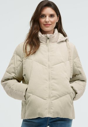 Beige corduroy puffer jacket with a high collar, side pockets, and a zipper closure. Features textured fabric and branded shoulder straps.
