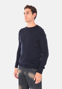 Maglione a maglia blu navy con scollatura rotonda, polsini e fondo a coste, e una texture liscia, abbinato a jeans in denim sbiaditi.
