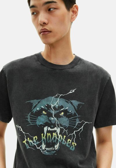 Juodas medvilninis marškinėliai su grafiką riaumojančio panteros su geltonomis akimis ir žaibo akcentais. Apvalus iškirpimas ir trumpomis rankov�ėmis.