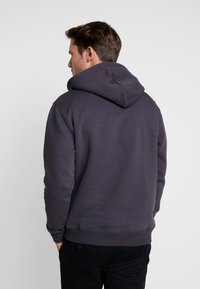 Sudadera gris oscuro hecha de tela suave, con una gran capucha, puños y dobladillo acanalados, y un corte relajado, vista desde la parte posterior.