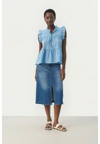 Ljusblå texturerad peplumtop med volangärmar, matchad med en midilång blå denimkjol med en framklippning och vita sandaler.