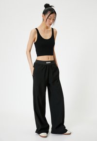 Zwarte geribde crop top met brede zwarte broek met een elastische tailleband. Het model draagt witte en tan schoenen, met haar in een bun gestyled.