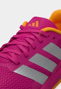 Φωτεινό ροζ αθλητικό παπούτσι με υφασμάτινο επάνω μέρος με υφή, γκρίζες ρίγες και πορτοκαλί λεπτομέρειες στη γλώσσα και την επένδυση. Τα κορδόνια είναι επίπεδα και ροζ.