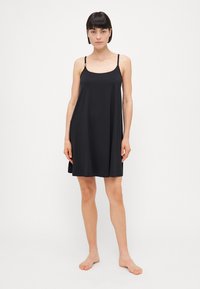 Vestido negro sin mangas con tirantes ajustables, dobladillo acampanado, textura suave y diseño minimalista. Sin patrones ni gráficos visibles.