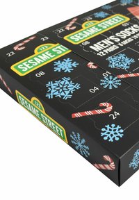 Scatola nera con fiocchi di neve e bastoncini di zucchero, etichettata "Sesame Street" e "Calze da uomo", con porte numerate per 12 paia di calze.