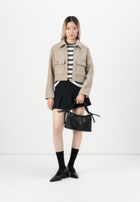 Beige cropped jacket with two front pockets, green and white striped shirt, black pleated skirt, black handbag, and black shoes with pointed toes.