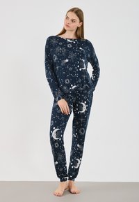 Ensemble de pyjama bleu marine comprenant un haut à manches longues et un pantalon. Le matériau présente un imprimé céleste avec des étoiles et des lunes. Tissu doux avec des poignets élastiques.