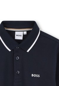 Mornarica polo majica s teksturiranim materialom, z belo prugasto ovratnikom, tremi gumbi in belim logotipom "BOSS" na levi prsni strani.