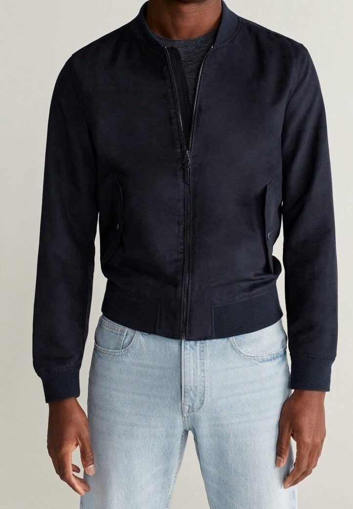 Homme portant une veste bomber noire ajustée avec une fermeture éclair avant, des poches à rabat, des poignets et un ourlet côtelés, associée à un jean bleu clair.