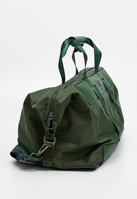 Zielona torba sportowa z nylonu z zamkiem błyskawicznym, regulowanym paskiem i podwójnymi uchwytami. Charakteryzuje się gładką fakturą i błyszczącym zielonym akcentem.
