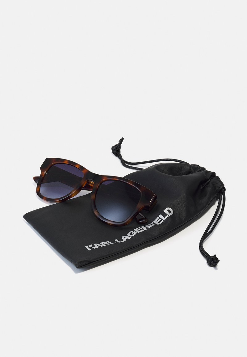 Schildkrötenmuster-Sonnenbrille mit verlaufsfarbenen Gläsern, auf einem schwarzen Kordelbeutel platziert, auf dem "KARL LAGERFELD" in weißer Schrift steht.