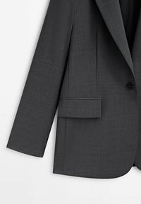 Blazer grigio scuro realizzato in tessuto texturizzato, chiusura frontale con un solo bottone, rever a notched e taschino sul lato sinistro.
