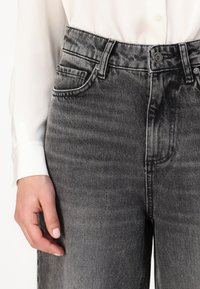 Jeans de mezclilla grises de tiro alto con un sutil patrón desgastado, diseño de cinco bolsillos y cierre de botón metálico en la parte delantera.