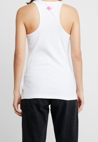 Top in bianco con design a schiena americana, caratterizzato da un accento di diamante rosa sulla parte superiore della schiena. Realizzato in tessuto morbido e elastico.