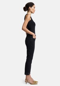 Schwarzes, eng anliegendes Tanktop, hochtaillierte schwarze Jeans mit umgeschlagenen Säumen und gelbe Slingback-Absätze mit Schlangenmotiv. Glatte Textur, minimalistisches Design.