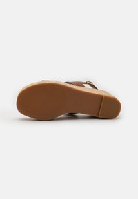 Brun kork høye sandaler med elastisk stropp, teksturert såle og en liten gullspenne, med en solid, sklisikker bunn.