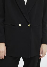 Černý blazer vyrobený z měkké látky. Disponuje dvouřadým zapínáním se dvěma zlatými knoflíky a bočními kapsami. Čisté linie a přiléhavý střih.