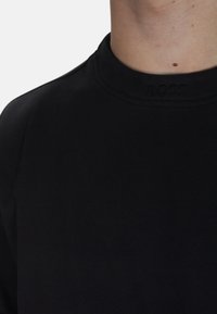 T-shirt nera in cotone con colletto a girocollo a costine, caratterizzata da logo "BOSS" in rilievo sul davanti, texture liscia e design aderente.