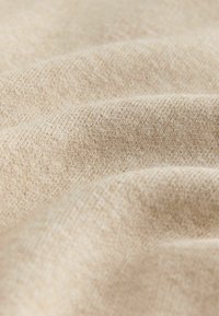 Tejido beige texturizado con una apariencia suave y entrelazada, que muestra sutiles variaciones en color y patrón, enfatizando su calidad táctil.