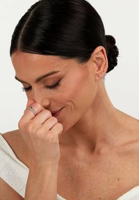 Silberner Ring mit einem verdrehten Design, mit einer zentralen Verzierung, getragen an einer Hand, die nahe dem Gesicht ruht. Der Hintergrund ist neutral.