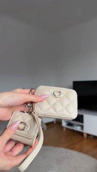 Sac à main en cuir matelassé beige avec une mini pochette, équipée de ferrures argentées, munie d'un fermoir ovale et d'une texture lisse, tenue par une main.