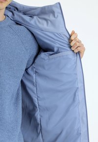 Jasnoniebieska ocieplana kurtka o gładkiej powierzchni, z jedną wewnętrzną kieszenią. Materiał wydaje się miękki i trwały.