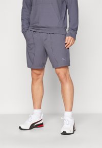 Grå atletiske shorts med sidelommer og et diskret sømdesign, båret med hvide sneakers med sorte og røde detaljer.