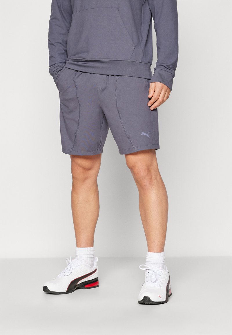 Grå atletiske shorts med sidelommer og et diskret sømdesign, båret med hvide sneakers med sorte og røde detaljer.