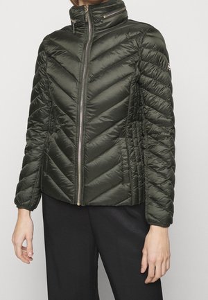 Dunkelgrüne gesteppte Jacke mit diagonaler Steppung, durchgehendem Reißverschluss vorne, hohem Kragen mit Reißverschlusstasche und langen Ärmeln an einer stehenden Person.