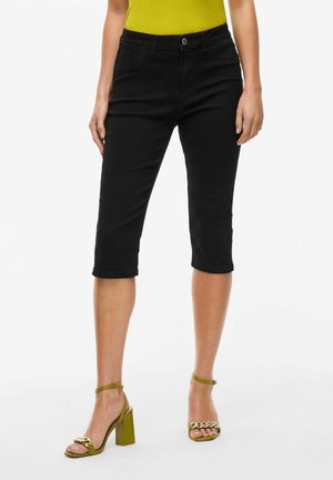 Zwarte knielange capri-broek van een rekbare katoenmix, met een sluiting aan de voorkant en voorzakken. Geaccentueerd door een groene top en hakken.