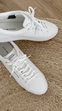 Weiße Leinensneaker mit runder Spitze, flacher Gummisohle und auffälligen Schnürsenkeln. Mit "TOMMY HILFIGER"-Logo auf der Lasche und der Seite. Einfaches Design.