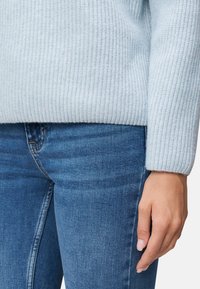 Himmelblaues geripptes Sweatshirt mit langen Ärmeln, kombiniert mit dunkelblauen Jeans. Die Textur ist weich und gestrickt, was den Komfort betont.