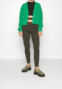 Zelený žebrovaný kardigan s detaily knoflíků, černý cropped top, olivově zelené slim kalhoty a masivní olivové loafers s černou podrážkou.