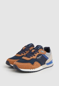 Zapatillas para hombre con malla azul marino y ante beige, detalles en gris y azul, y suela de goma texturizada. Diseño con cordones y logotipo.